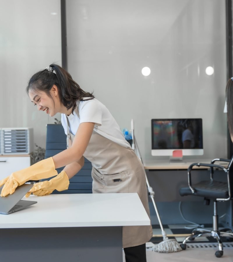 Two Asian housekeepers wear overalls and work together efficiently to clean the living room, study